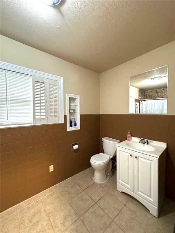 bathroom featuring a textured ceiling, vanity, tile patterned floors, toilet, and tile walls