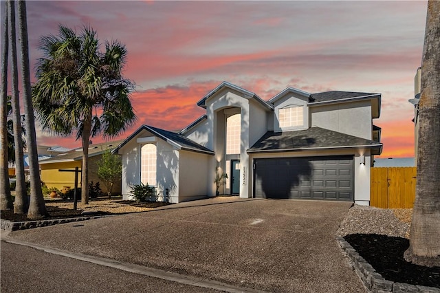 view of front of home with driveway, a shingled roof, fence, and stucco siding