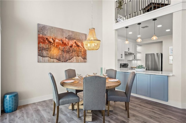 dining space featuring a towering ceiling, wood finished floors, visible vents, and baseboards