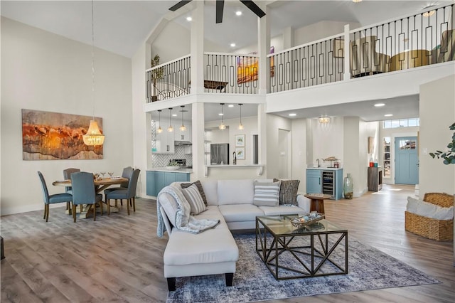 living area with ceiling fan, wine cooler, wood finished floors, and a high ceiling