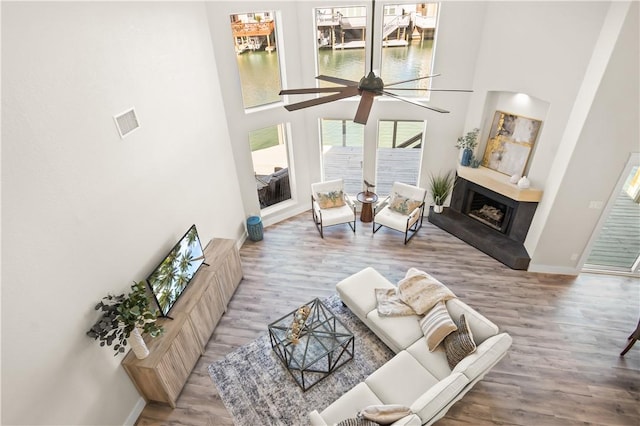 living area with a fireplace with raised hearth, a towering ceiling, baseboards, and wood finished floors