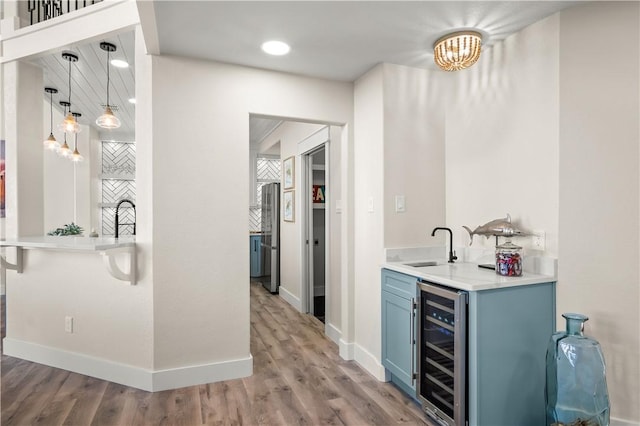 bar with light wood-type flooring, beverage cooler, baseboards, and a sink