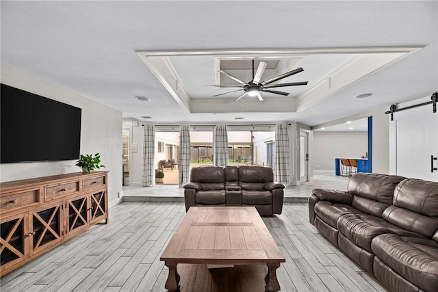 living room featuring a raised ceiling, a barn door, ceiling fan, and ornamental molding