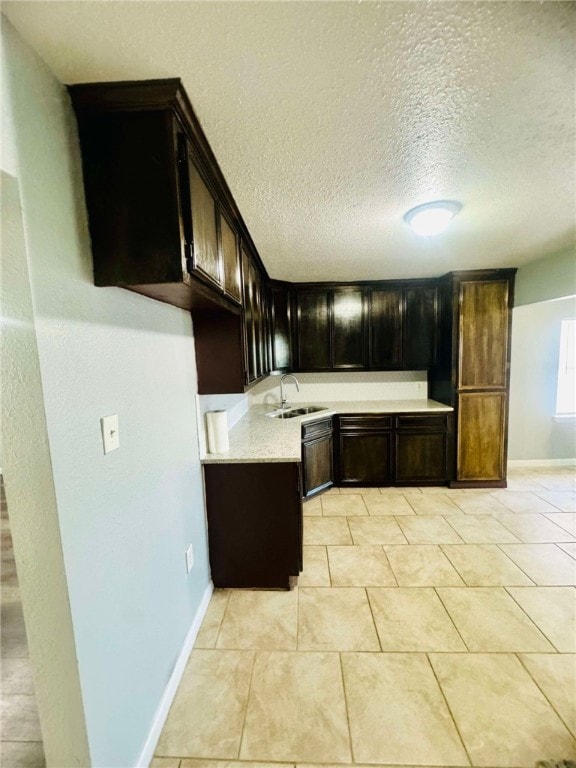 kitchen with baseboards, light stone countertops, light tile patterned floors, a textured ceiling, and a sink