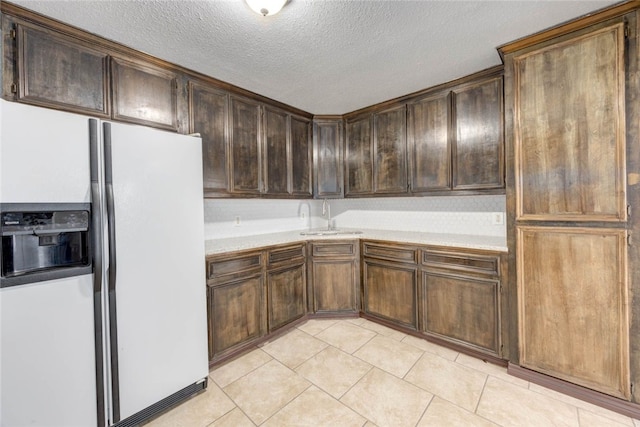 kitchen featuring light tile patterned floors, a sink, light countertops, dark brown cabinets, and white fridge with ice dispenser