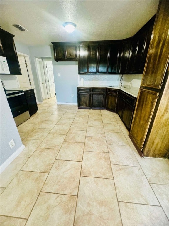 kitchen featuring stainless steel electric stove, sink, light tile patterned floors, and a textured ceiling