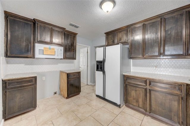 kitchen with white appliances, light stone counters, visible vents, decorative backsplash, and dark brown cabinets