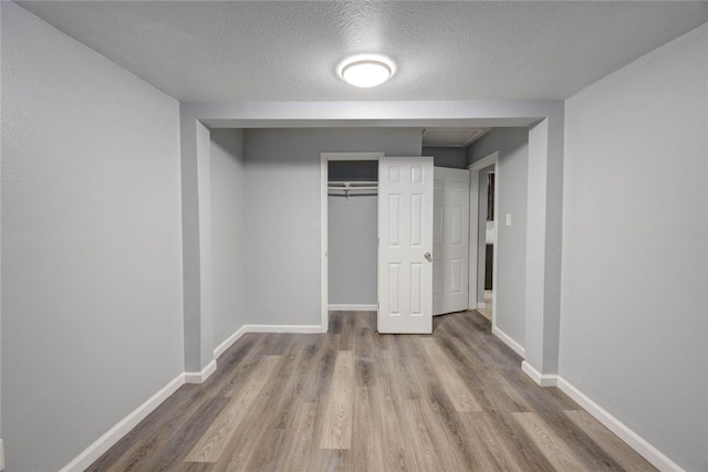 unfurnished bedroom featuring a closet, baseboards, a textured ceiling, and wood finished floors