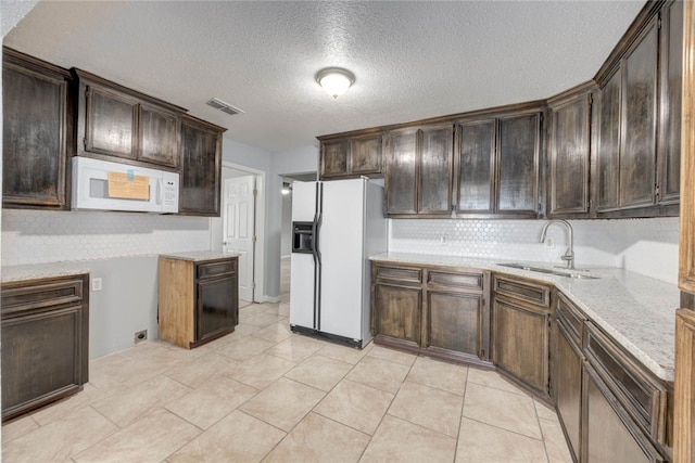 kitchen featuring white appliances, dark brown cabinets, visible vents, and a sink