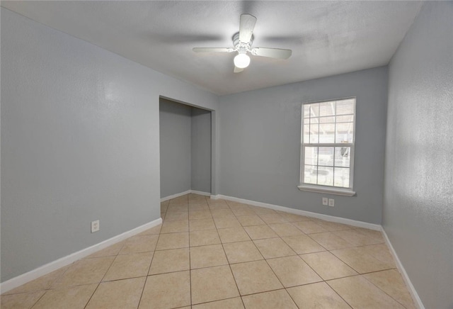 unfurnished room with baseboards, ceiling fan, light tile patterned flooring, and a textured wall