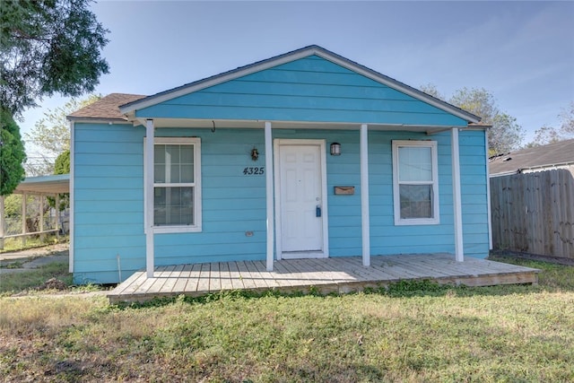 bungalow-style house featuring a carport, covered porch, a front yard, and fence