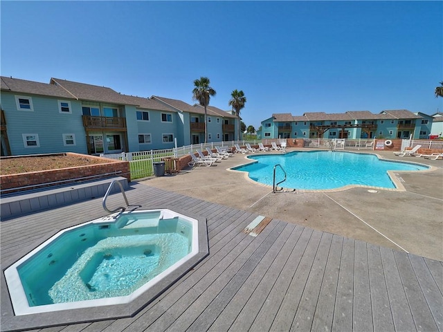 pool with a residential view, a wooden deck, fence, a community hot tub, and a patio