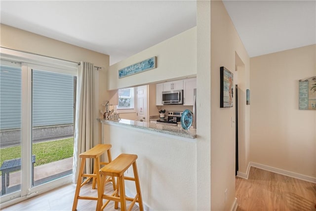 kitchen with baseboards, light wood-style floors, a breakfast bar area, white cabinets, and appliances with stainless steel finishes