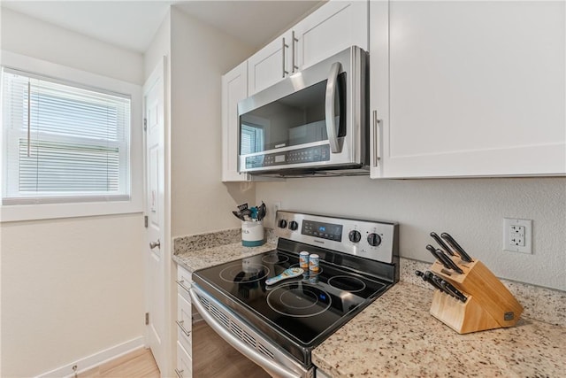 kitchen with baseboards, white cabinets, light stone countertops, and stainless steel appliances