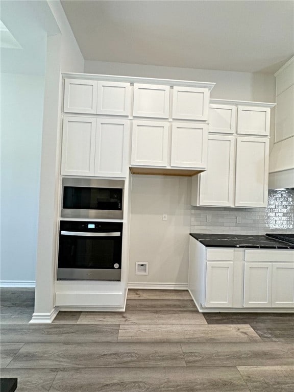 kitchen featuring stainless steel appliances, white cabinetry, light wood-type flooring, and tasteful backsplash