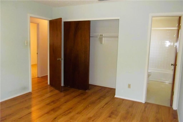 unfurnished bedroom featuring wood finished floors, a closet, and connected bathroom