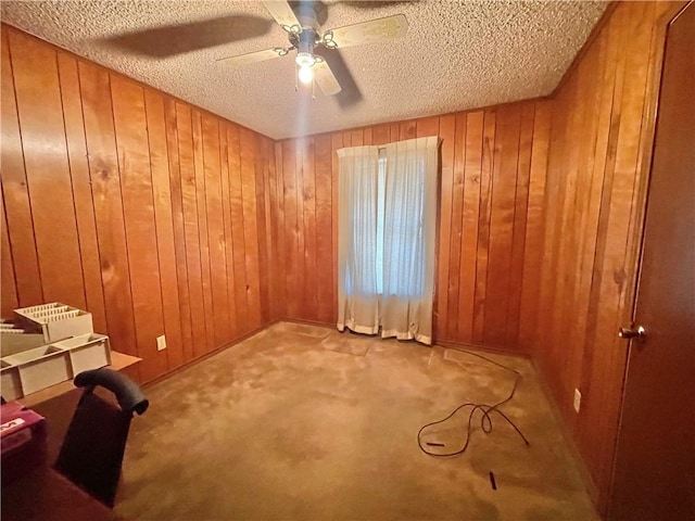 carpeted empty room with ceiling fan, wood walls, and a textured ceiling