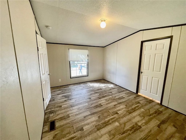 unfurnished bedroom featuring wood finished floors, ornamental molding, lofted ceiling, and visible vents