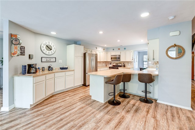 kitchen with a peninsula, a breakfast bar, white cabinetry, light wood finished floors, and stainless steel appliances