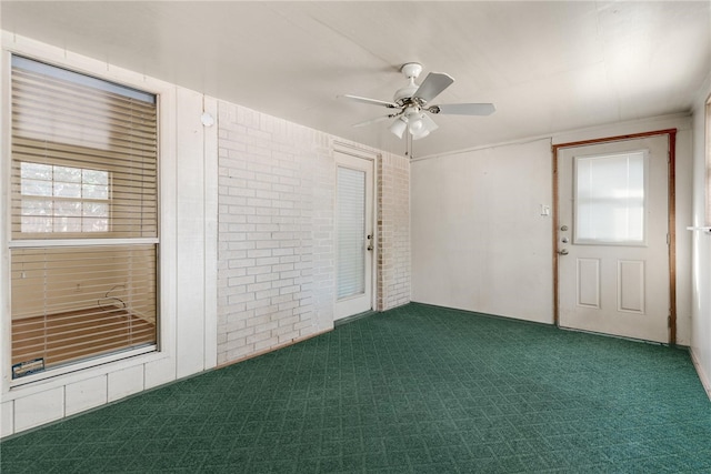 empty room featuring brick wall, ceiling fan, and dark carpet