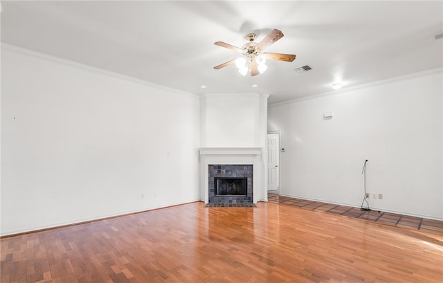 unfurnished living room with light wood-type flooring, a tiled fireplace, ceiling fan, and ornamental molding