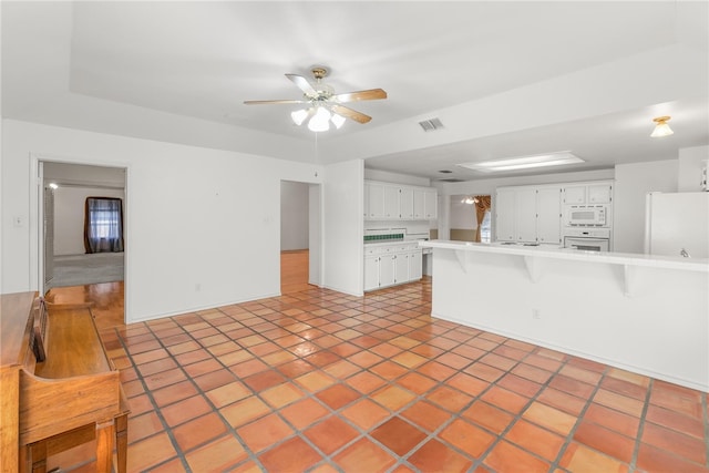 kitchen featuring white cabinetry, kitchen peninsula, a kitchen breakfast bar, ceiling fan, and white appliances