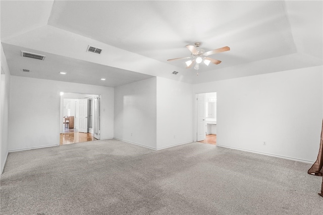 carpeted spare room featuring a tray ceiling and ceiling fan