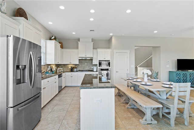 kitchen featuring a center island with sink, tasteful backsplash, light tile patterned flooring, white cabinetry, and appliances with stainless steel finishes