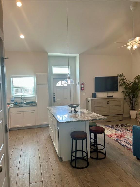 15110 Arashi Beach Dr, Corpus Christi, TX 78418 - kitchen with light wood-style flooring, a kitchen island, ceiling fan, white cabinetry, and light stone countertops