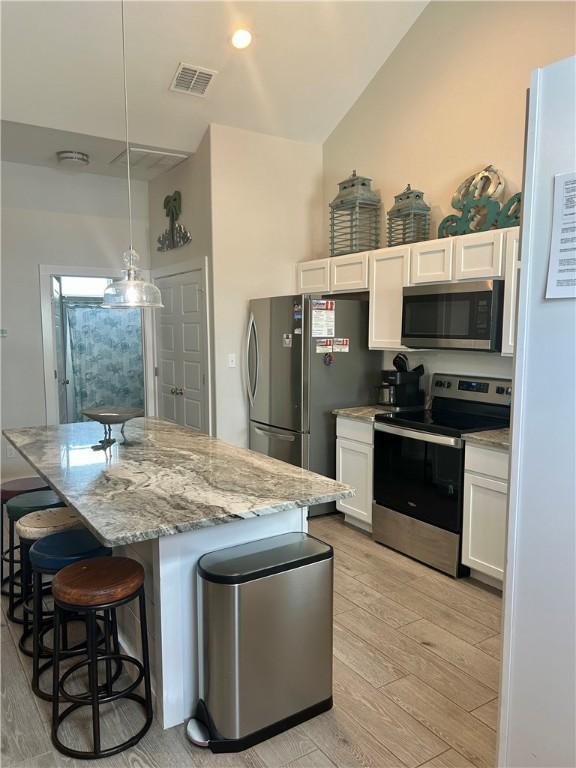 15110 Arashi Beach Dr, Corpus Christi, TX 78418 - kitchen featuring stainless steel appliances, light wood-type flooring, white cabinets, and light stone counters