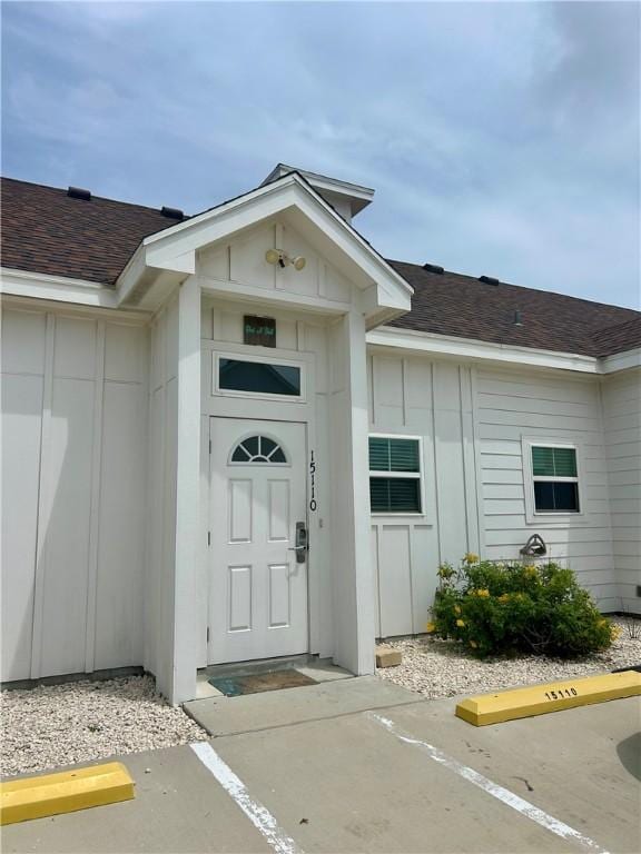15110 Arashi Beach Dr, Corpus Christi, TX 78418 - doorway to property featuring board and batten siding, roof with shingles, and uncovered parking