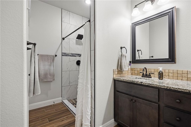 1570 Maryville Loop, Beeville, TX 78102 - bathroom featuring wood finished floors, decorative backsplash, vanity, a tile shower, and baseboards