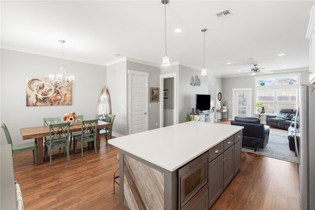 kitchen with appliances with stainless steel finishes, ornamental molding, ceiling fan with notable chandelier, a kitchen island, and dark hardwood / wood-style flooring