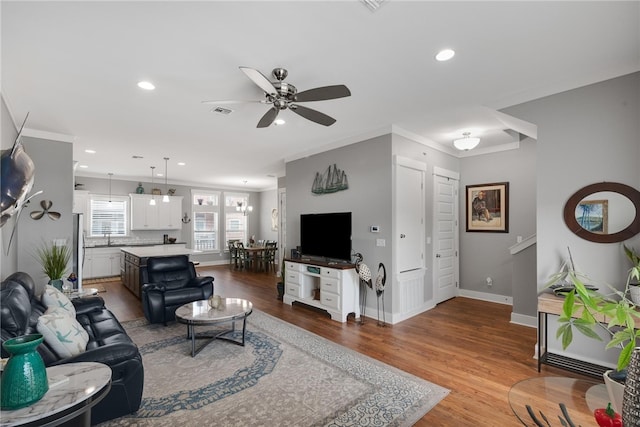 living room featuring light hardwood / wood-style flooring, ceiling fan, crown molding, and sink