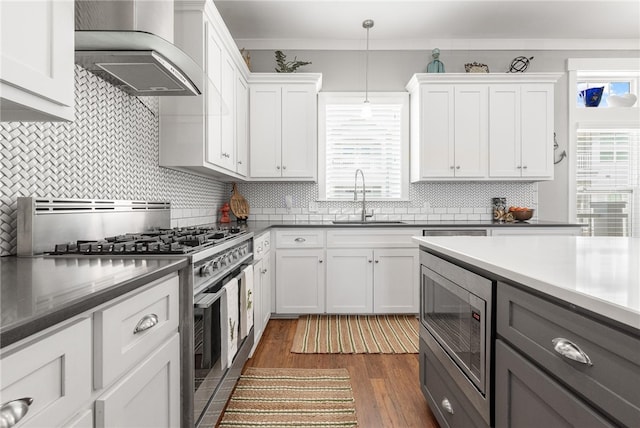 kitchen with stainless steel appliances, white cabinetry, pendant lighting, sink, and wall chimney exhaust hood