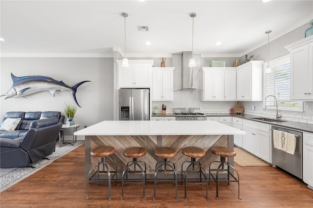 kitchen featuring stainless steel appliances, hanging light fixtures, wall chimney exhaust hood, and a kitchen island