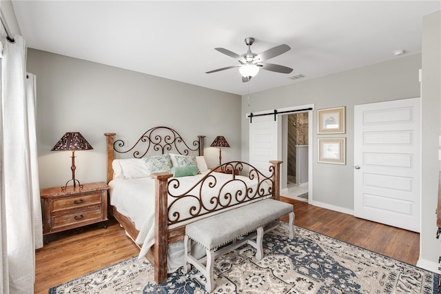 bedroom with a barn door, hardwood / wood-style flooring, and ceiling fan