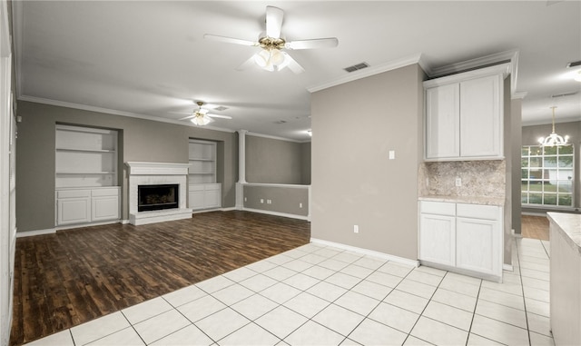 unfurnished living room with crown molding, light tile patterned flooring, ceiling fan with notable chandelier, and a brick fireplace