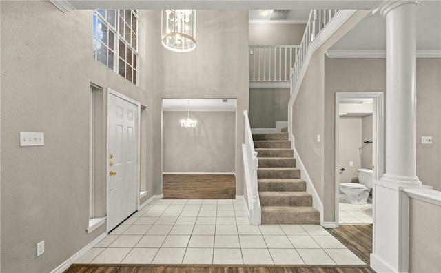 foyer with a towering ceiling, decorative columns, a notable chandelier, crown molding, and light hardwood / wood-style flooring