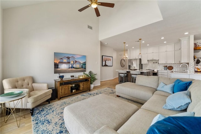living area with recessed lighting, light wood-type flooring, a high ceiling, visible vents, and a ceiling fan