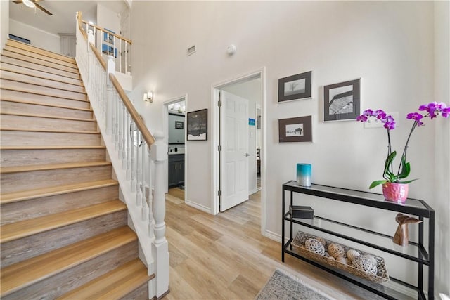 stairs with baseboards, a high ceiling, visible vents, a ceiling fan, and wood finished floors