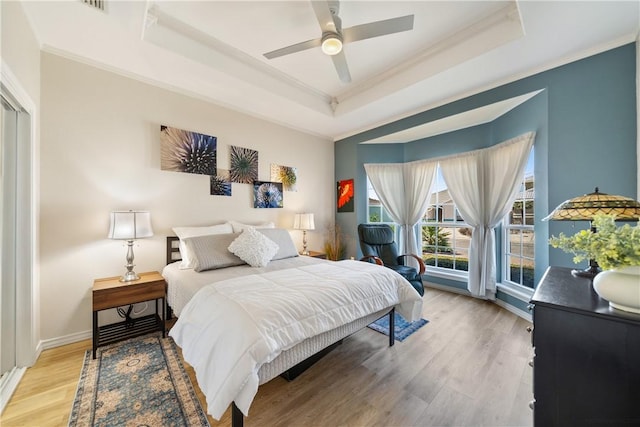 bedroom with a tray ceiling, crown molding, and light wood-type flooring