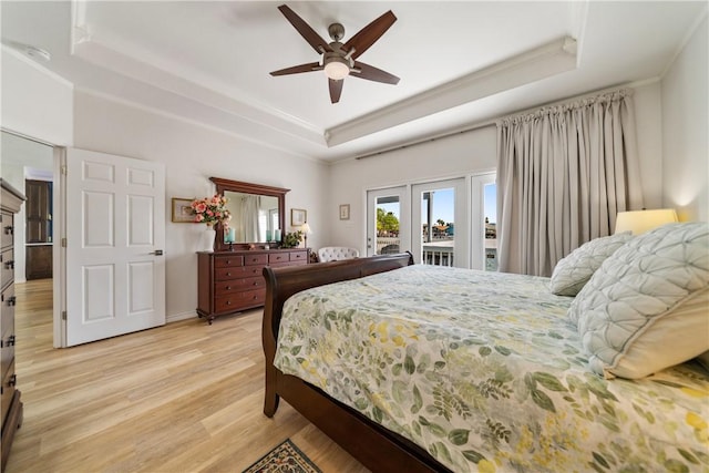 bedroom featuring access to exterior, french doors, light wood finished floors, and a raised ceiling