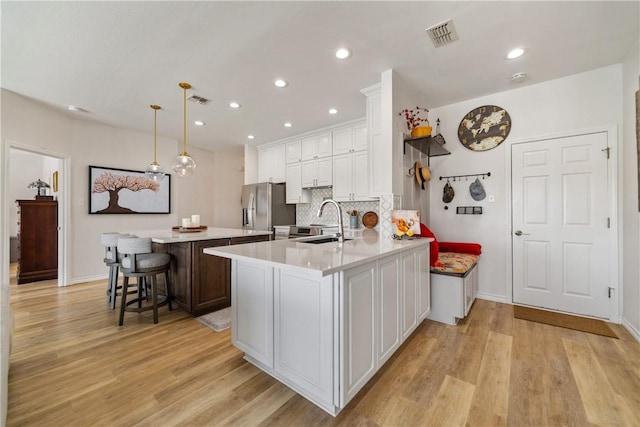 kitchen with white cabinetry, light countertops, a sink, light wood-style floors, and freestanding refrigerator