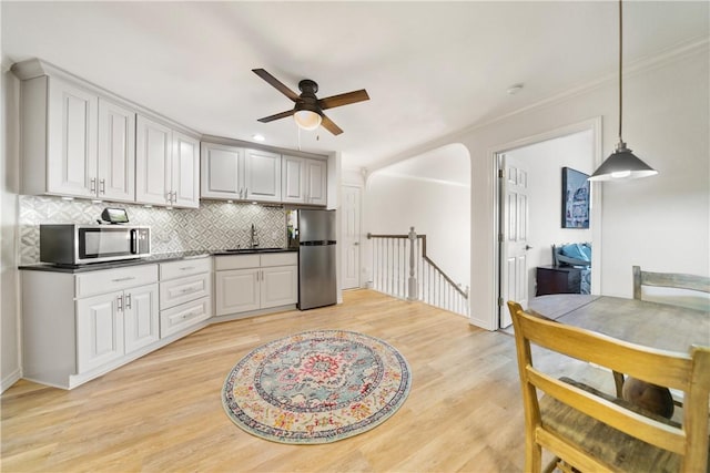 kitchen featuring a sink, a ceiling fan, light wood finished floors, stainless steel appliances, and decorative backsplash