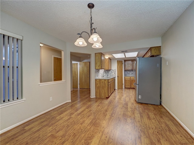 kitchen with sink, tasteful backsplash, light hardwood / wood-style floors, an inviting chandelier, and stainless steel fridge