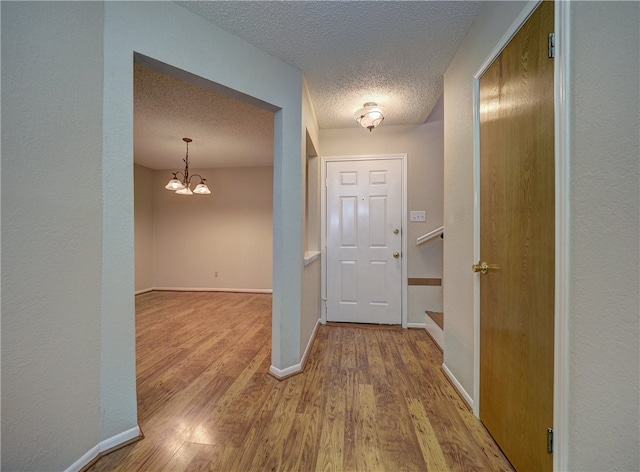 hallway featuring hardwood / wood-style floors, a textured ceiling, and an inviting chandelier