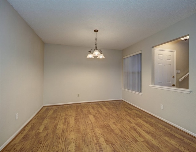 unfurnished room featuring hardwood / wood-style floors, a textured ceiling, and an inviting chandelier