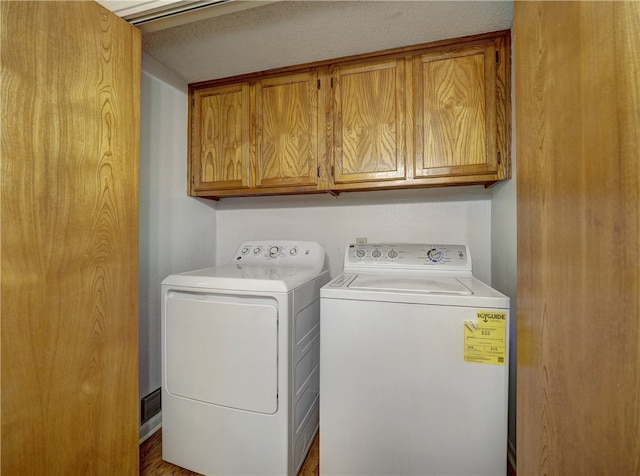 laundry area featuring cabinets, a textured ceiling, washing machine and dryer, and wood-type flooring