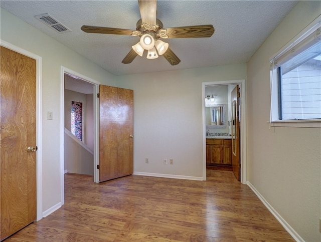 unfurnished bedroom featuring ensuite bath, ceiling fan, wood-type flooring, and a textured ceiling